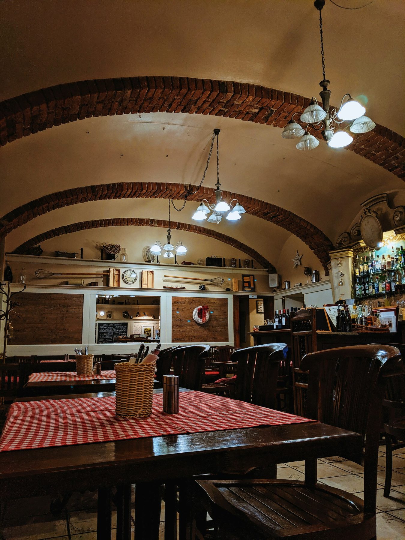 Sala di trattoria sotto una volta di mattoni, tavoli con tovaglie a quadri rossi
